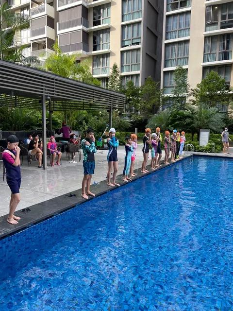 A group of children in goggles lined up at the pool edge for a group training session