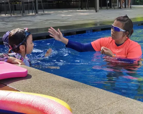 Coach Jina demonstrating hand position to a swimmer at the pool wall